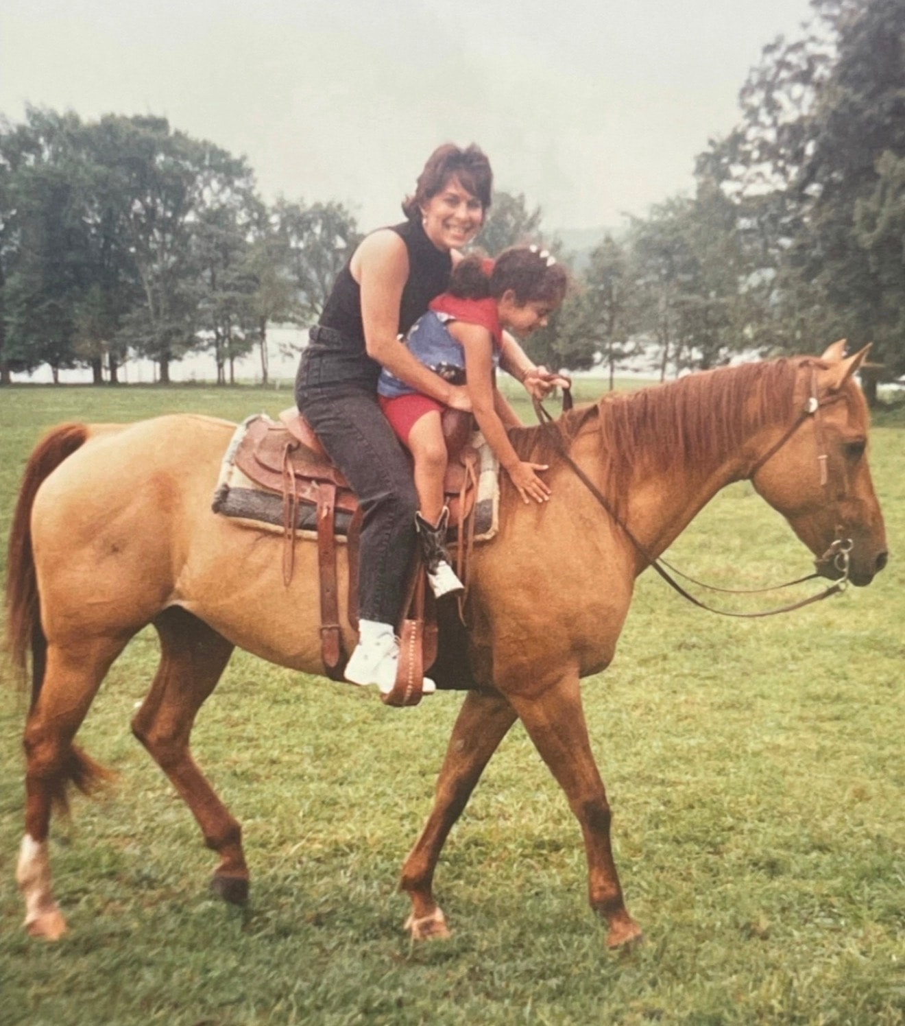 Mother and daughter riding a horse together in a grassy field